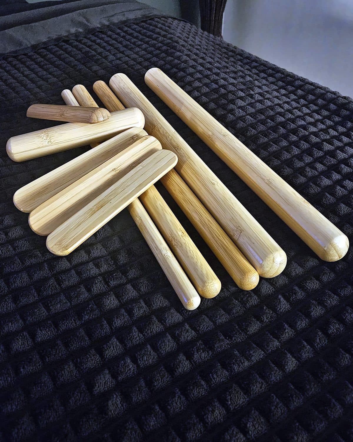 Byron's set of smooth bamboo massage sticks laid out on a dark quilted treatment table at TCH Massage