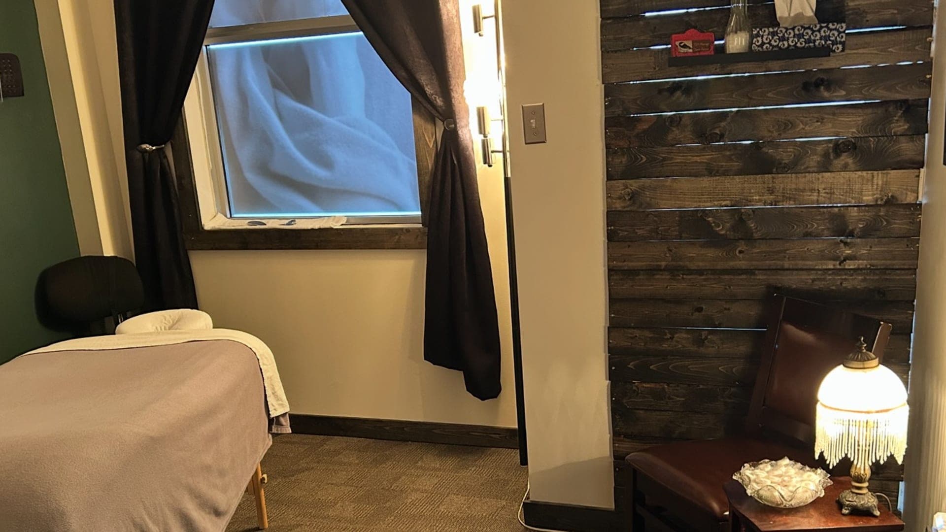 Treatment room with a massage table, lamp and wood feature wall at TCH Massage in Olds
